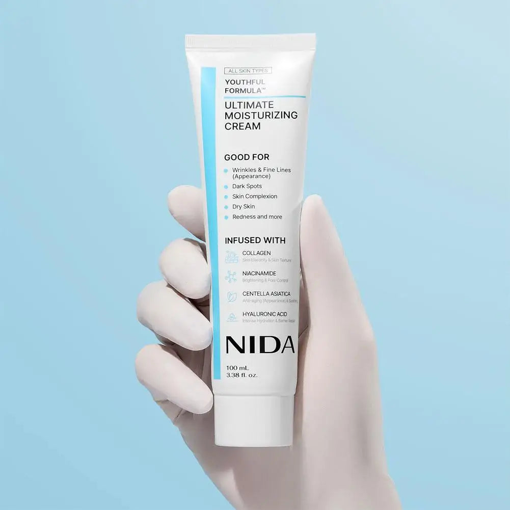 Hand holding a tube of NIDA Ultimate Moisturizing Cream against a light blue background