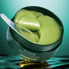 Green eye mask in a jar with a spoon on a reflective surface