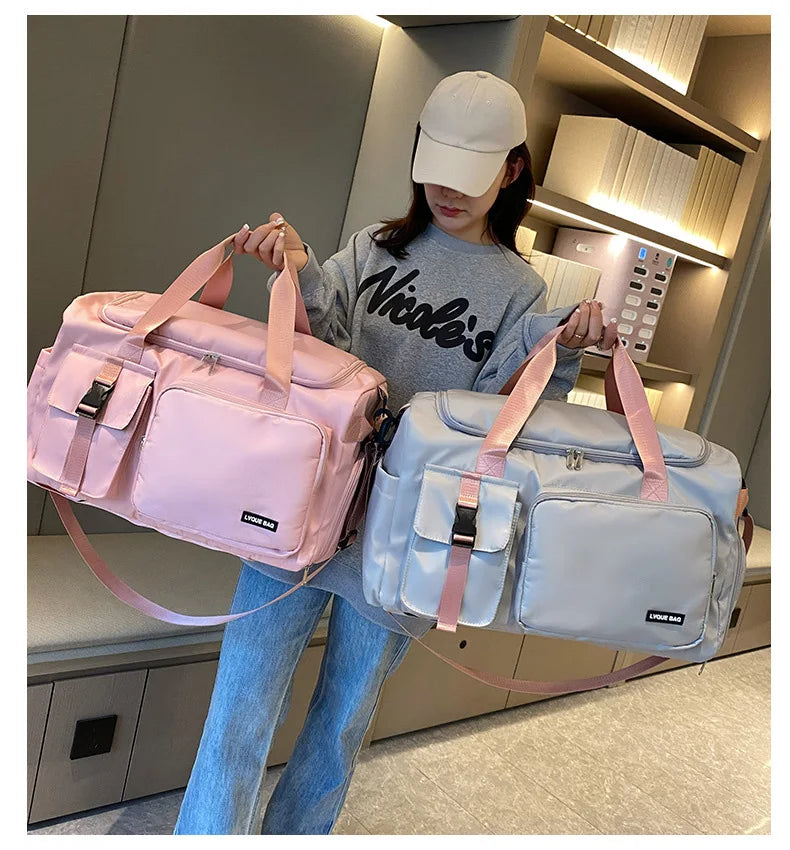 Person holding two duffel bags, one pink and one gray, in a room.